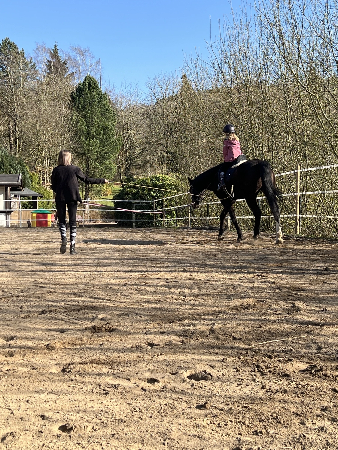 Pferderanch Sauerland – eine Frau hilft einem Kind beim Reiten in einer Reithalle